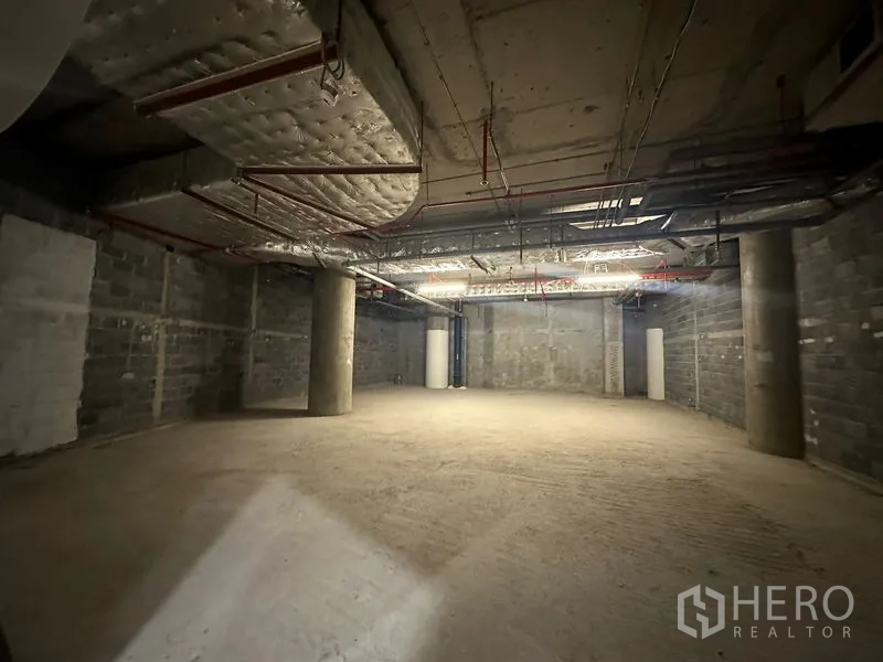 Retail Space for rent - Bare-shell retail unit with open floor, concrete columns, exposed ducting and fire sprinkler lines.