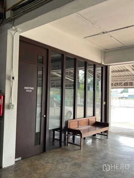 Warehouse for sale in Bang Bua Thong, Nonthaburi - Glass-front meeting room off the loading area with a wooden bench outside.