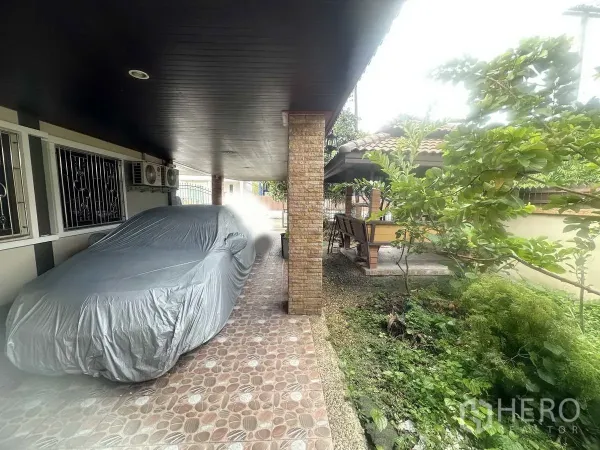 Detached House for sale in Pathum Thani - Covered two-car carport beside greenery and a path leading toward the garden pavilion.