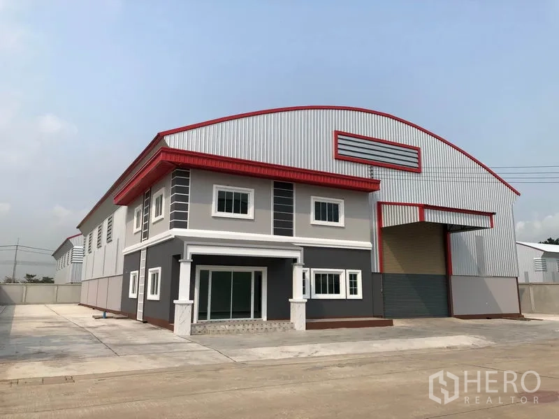 Factory for rent or sale in Bang Len, Nakhon Pathom - Angled exterior view of factory showing long facade, driveway and parking area.
