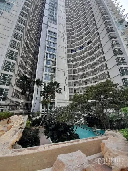 Condominium for rent or sale in Pathum Wan, Bangkok - Modern high‑rise condominium exterior with curved facade, palm trees, and a pool garden.