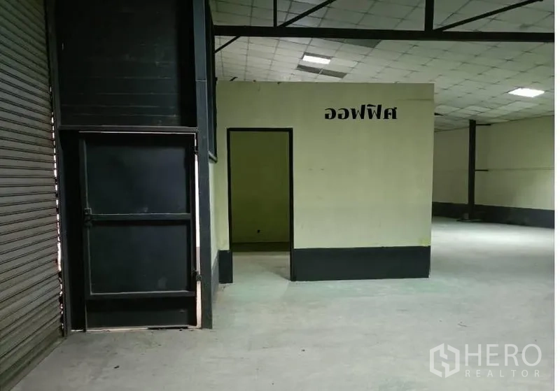 Warehouse for rent in Bang Khen, Bangkok - Internal office room beside a large shutter door inside the warehouse.