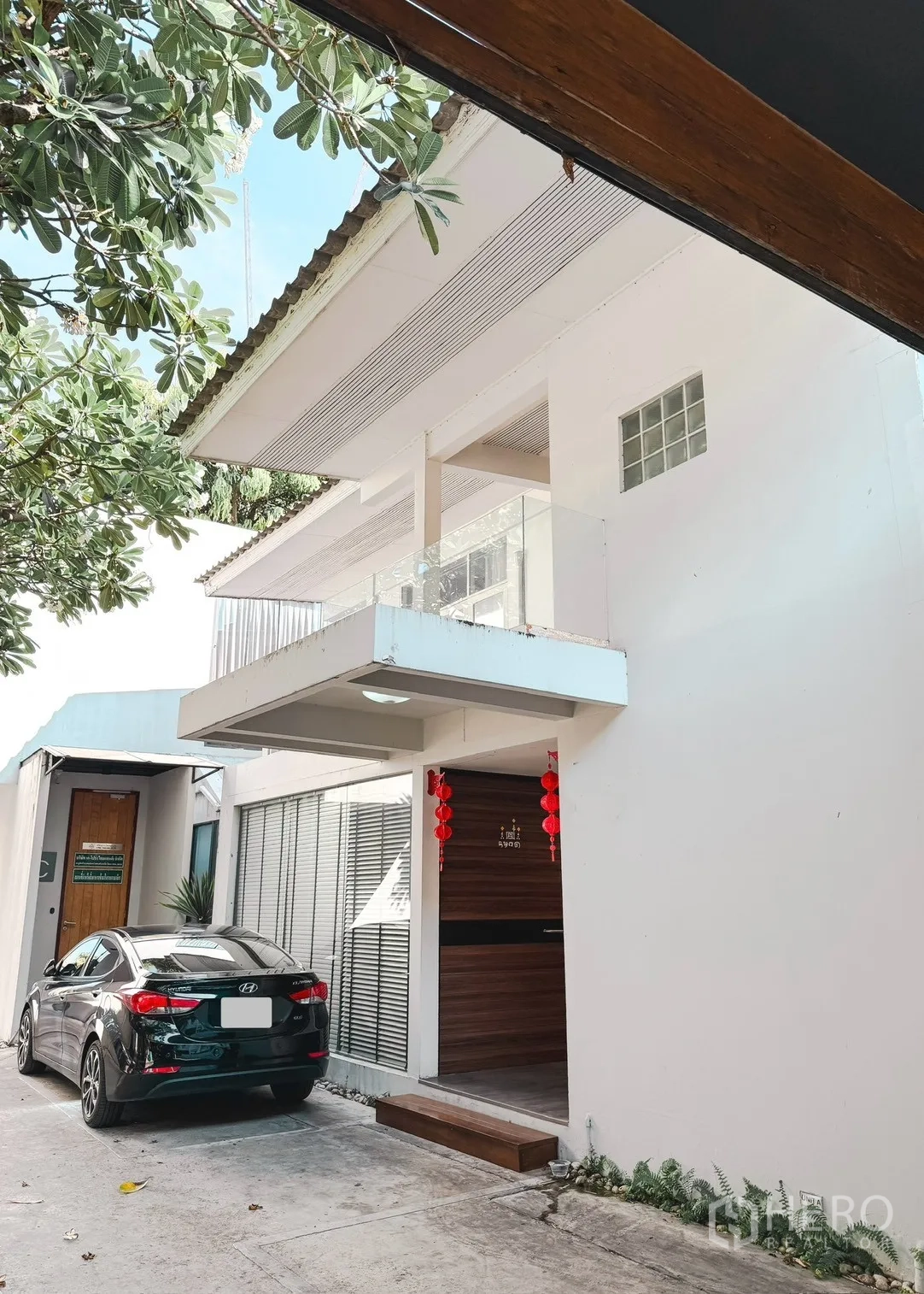 Home Office for rent in Watthana, Bangkok - Modern white home office exterior with balcony, driveway and on-site parking under leafy trees.