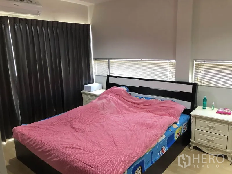 Townhouse for rent or sale in Suan Luang, Bangkok - Guest bedroom with double bed, pink duvet, blackout curtains and corner windows with blinds.