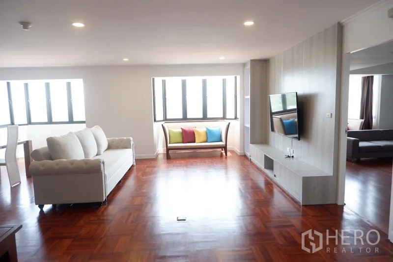 Condominium for rent in Khlong Toei, Bangkok - Bright condo living room with hardwood floors, white sofa, TV wall and a bay window bench.