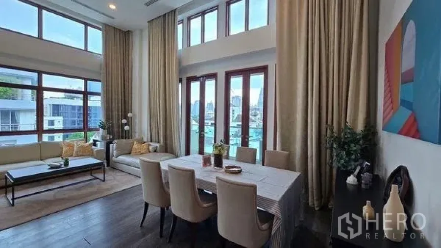 Condominium for rent in Pathum Wan, Bangkok - Alternate angle of the double-height living and dining space with tall drapes and windows.