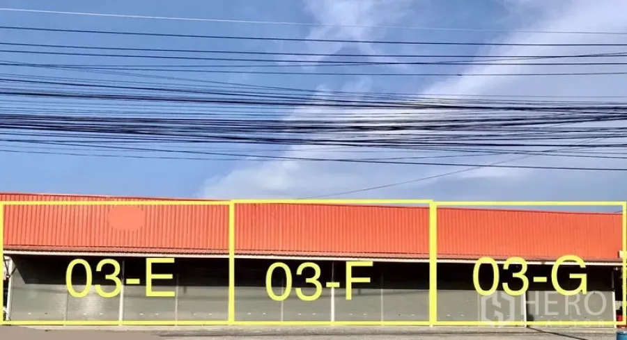 คลังสินค้า ให้เช่าในPathum Thani - โกดังหน้ากว้างหลังคาสีส้ม มีประตูม้วนหลายช่องระบุ 03‑E, 03‑F และ 03‑G พร้อมพื้นที่หน้าร้านกว้าง.