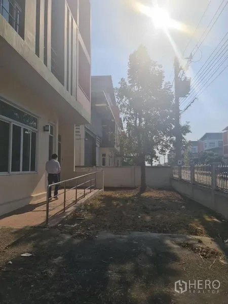 Factory for rent or sale in Lam Luk Ka, Pathum Thani - Front yard with walkway, tree, perimeter fence and afternoon sun.
