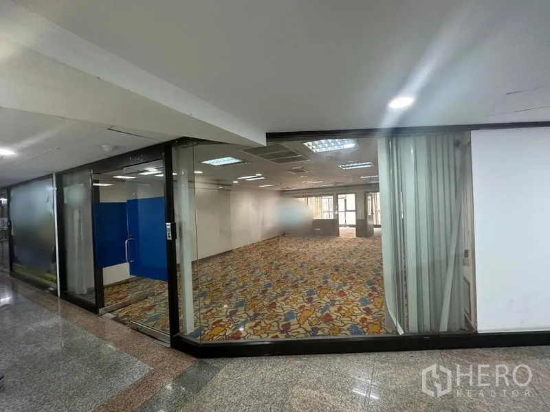 Office Space for rent - Corner office with floor-to-ceiling glass frontage, bright ceiling lights and patterned carpet, viewed from the corridor.