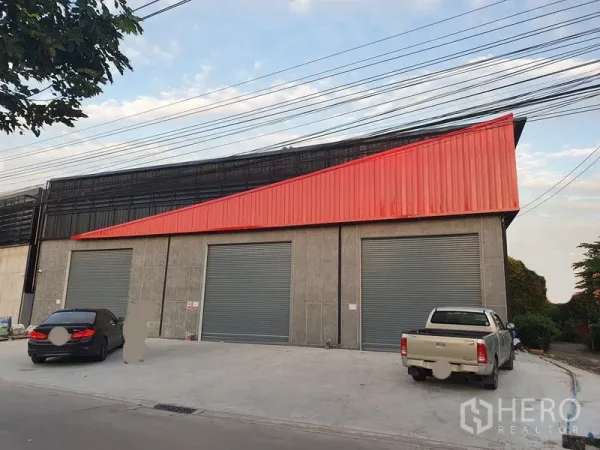 货栈 出租在Pak Kret, Nonthaburi - 正立面展示三个大型灰色卷闸门，前方为宽广混凝土停车区。