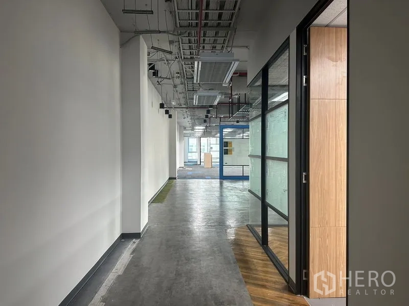 Office Space for rent in Bang Rak, Bangkok - Long corridor in a modern office showing exposed services and a glass wall.