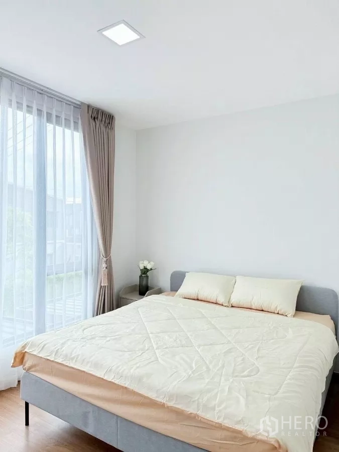 Townhouse for rent in Bang Phli, Samut Prakan - Master bedroom with double bed by full-height windows and bedside table.