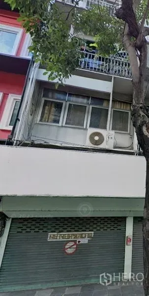 Shophouse for rent in Khlong Toei, Bangkok - Multi-storey shophouse facade with green roller shutter, balcony and street tree in the Sukhumvit area.