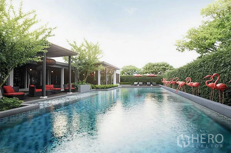 Townhouse for sale in Suan Luang, Bangkok - Communal swimming pool with shaded pavilion, hedges, and sun loungers.