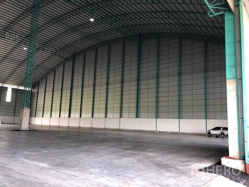 Warehouse for rent in Sai Noi, Nonthaburi - Huge covered bay with arched roof; a car parked along the wall shows scale.