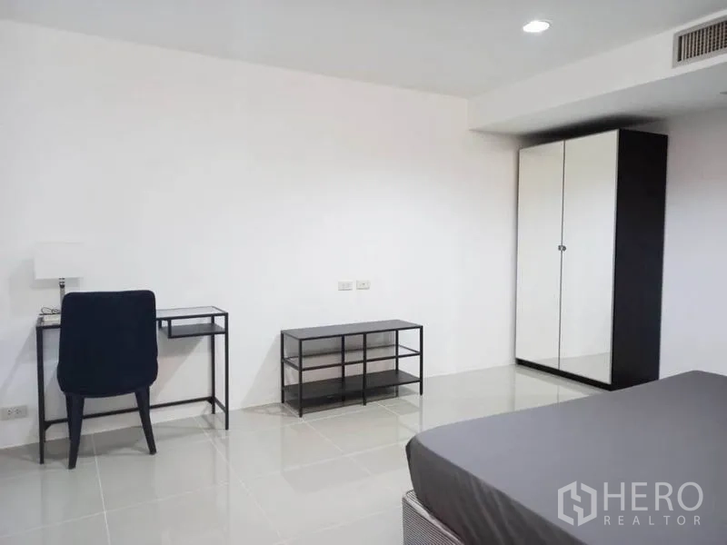 Condominium for rent in Khlong Toei, Bangkok - Spacious bedroom with a desk, black chair, media console and mirrored wardrobe.