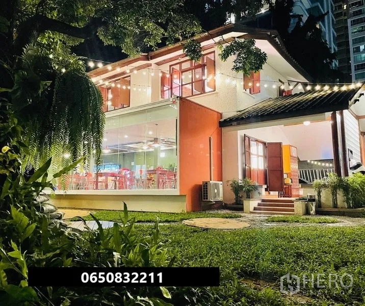 零售空间 出租在Pathum Wan, Bangkok - 夜间两层玻璃店屋，草坪与串灯点缀。
