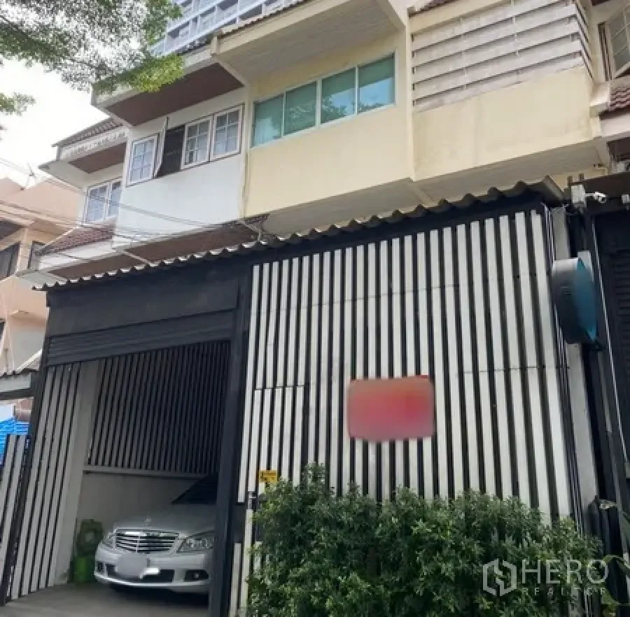 Townhouse for rent in Watthana, Bangkok - Townhouse exterior in Watthana, Bangkok with striped gate, covered carport and greenery.