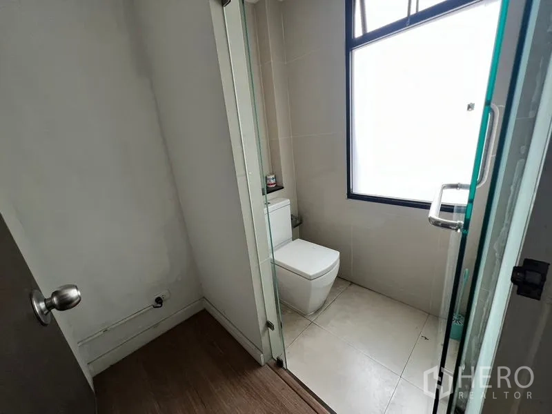 Townhouse for rent or sale in Khlong Toei, Bangkok - Guest bathroom with toilet and glass shower partition and a large frosted window.