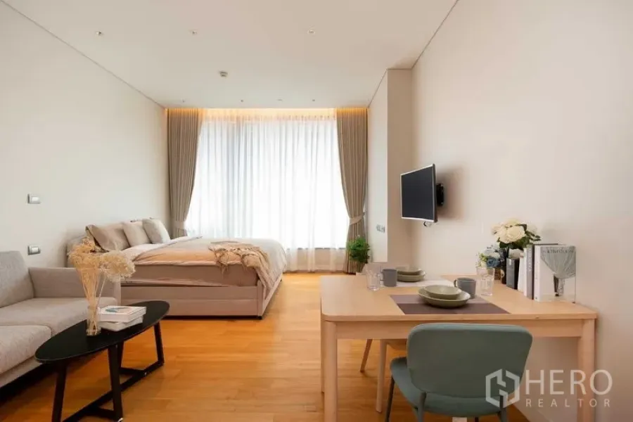 Condominium for rent in Pathum Wan, Bangkok - Open-plan layout showing dining for two, mounted TV and a bright window in a compact condo.