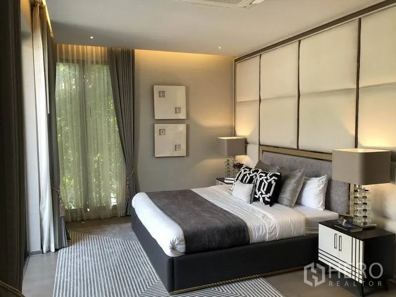 Detached House for sale in Bang Kapi, Bangkok - Primary bedroom with padded feature wall, large windows, sheer curtains and soft ambient lighting.