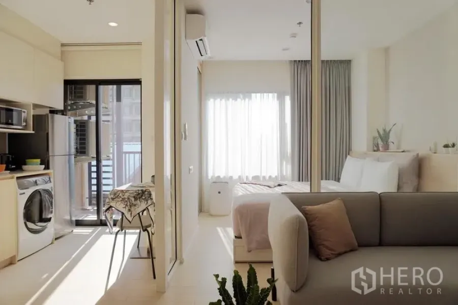 Condominium for rent in Pathum Wan, Bangkok - Sunny open-plan Bangkok condo with kitchenette, washer, and glass-partitioned bedroom near the balcony.