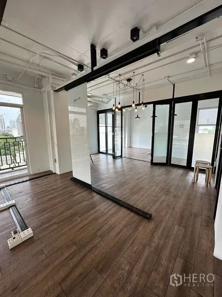 Office Space for rent in Watthana, Bangkok - Open workspace with sliding glass doors, exposed ceiling pipes, pendant chandelier, and access to a small balcony.