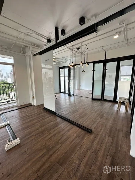 Office Space for rent in Watthana, Bangkok - Open workspace with sliding glass doors, exposed ceiling pipes, pendant chandelier, and access to a small balcony.