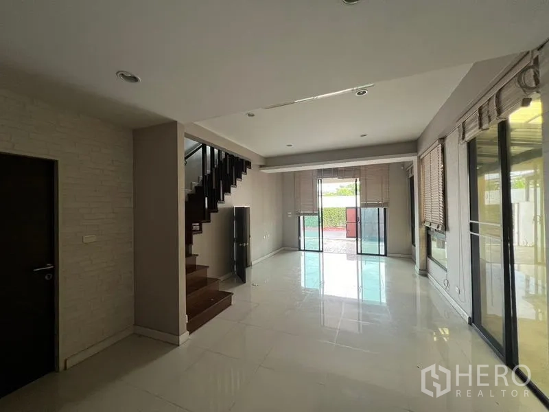 Townhouse for rent or sale in Khlong Toei, Bangkok - Open-plan living area with glossy tile floors, staircase and wide sliding doors.