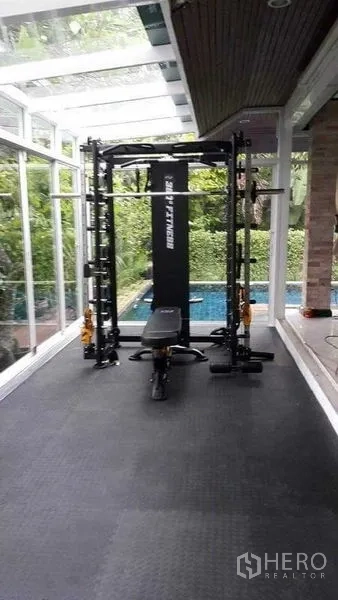 Detached House for sale in Bang Na, Bangkok - Home gym with multi-function weight machine in a bright glass sunroom by the pool.