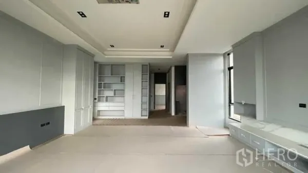 Detached House for sale in Mueang Nonthaburi, Nonthaburi - Spacious living room with built‑in shelves, tall windows and light grey cabinetry.
