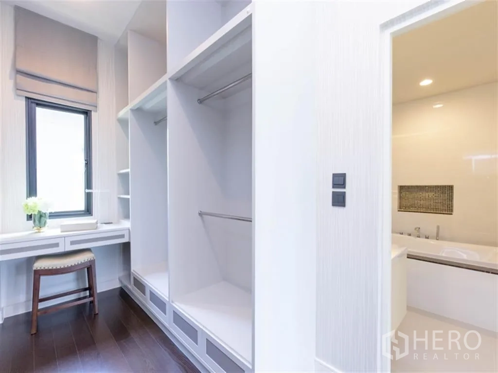 Detached House for rent in Bang Kapi, Bangkok - Walk-in closet with built-in shelves and dressing table leading to a bathroom with bathtub.
