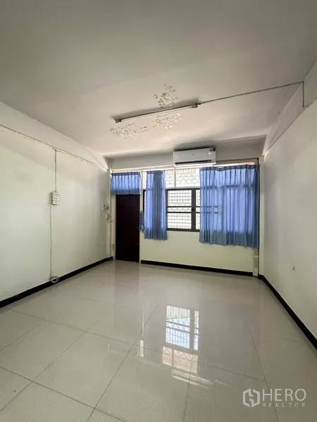 Shophouse for rent or sale in Phra Khanong, Bangkok - Air-conditioned bedroom with large window, blue curtains, and glossy white floor tiles.
