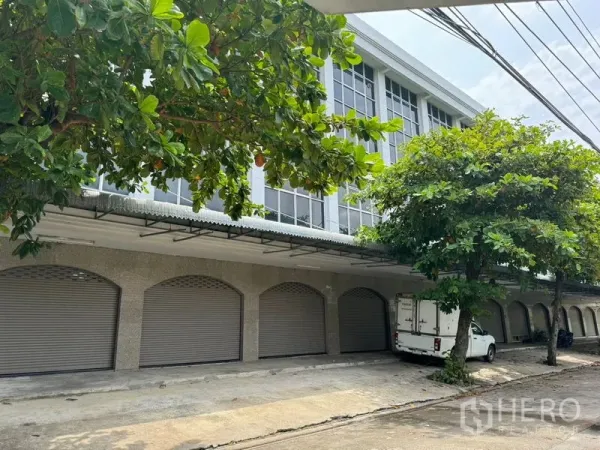 Shophouse for rent in Khlong Toei, Bangkok - Multi-bay shophouse exterior with roller shutters, loading canopy and leafy trees near BTS On Nut in Bangkok.