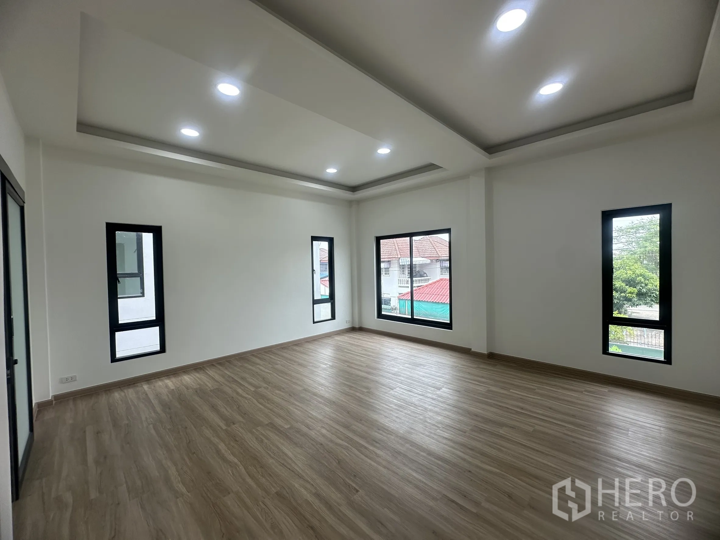 Warehouse for sale in Khlong Luang, Pathum Thani - Bright office space with multiple tall windows and laminate floors overlooking the neighborhood.