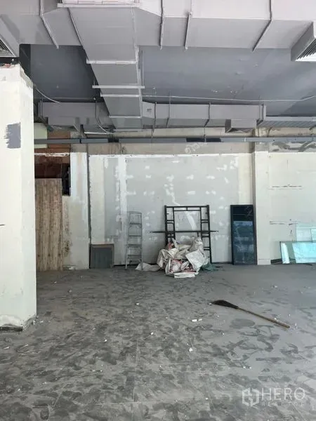 Retail Space for rent in Khlong Toei, Bangkok - Unfinished shop space with high ceilings, ladder and renovation materials, offering a flexible open-plan layout for retail use.