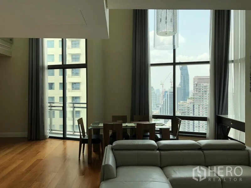 Condominium for rent or sale in Khlong Toei, Bangkok - Dining area by floor-to-ceiling windows and balcony with Bangkok skyline views.