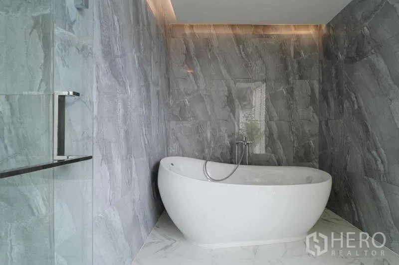 Townhouse for rent or sale in Watthana, Bangkok - Luxury bathroom with freestanding oval bathtub and gray stone walls.