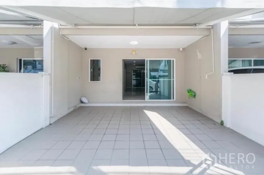 Townhouse for rent or sale in Watthana, Bangkok - Covered carport with tiled floor and sliding glass entrance to the townhouse.