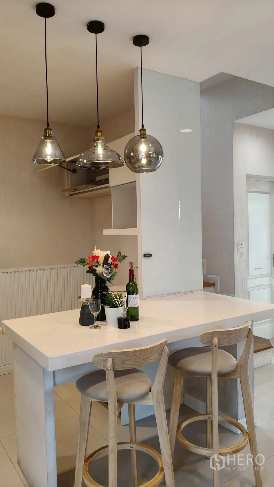Detached House for rent or sale in Mueang Samut Prakan, Samut Prakan - Kitchen island with white countertop, three pendant lights and bar stools, styled with flowers.