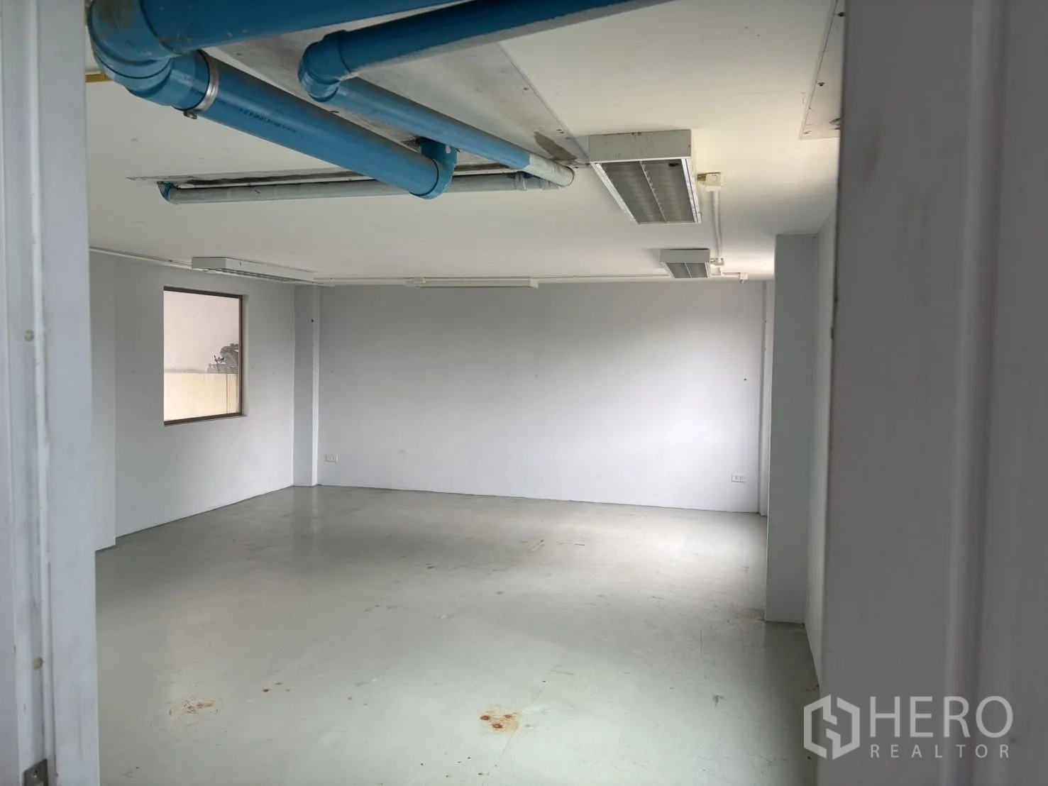 Warehouse for rent or sale in Wang Thonglang, Bangkok - Empty office room with exposed blue ceiling pipes and fluorescent lights.