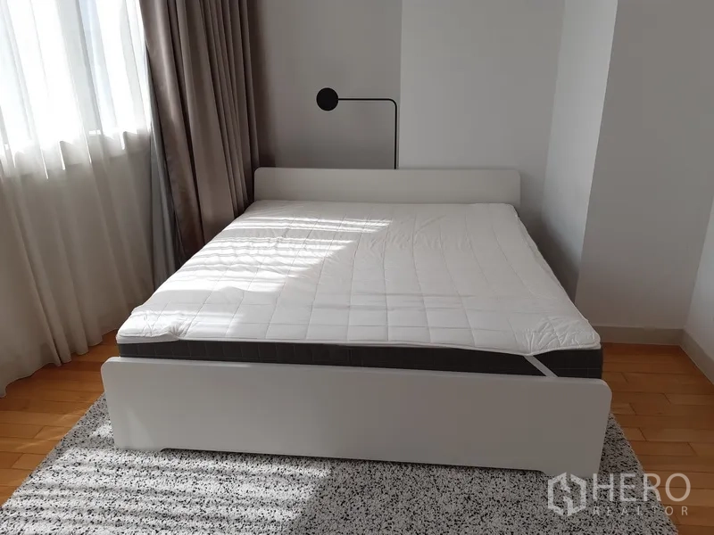 Condominium for rent in Khlong Toei, Bangkok - Sunlit bedroom with white bed, bedside lamp and curtains.