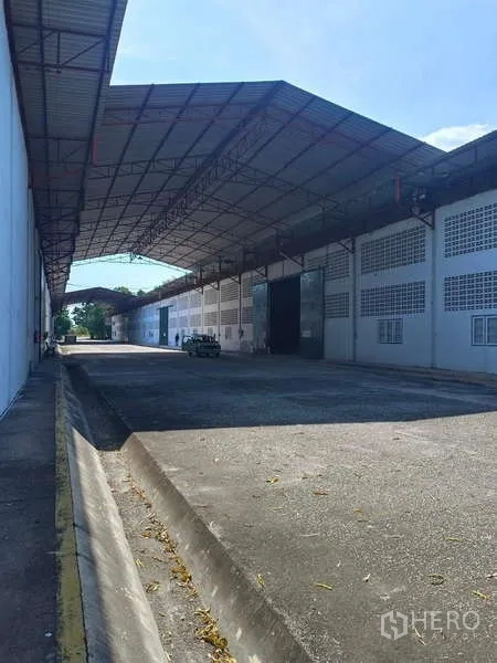 Warehouse for rent in Mueang Rayong, Rayong - Shaded loading area along the warehouse wall with curb and drainage.