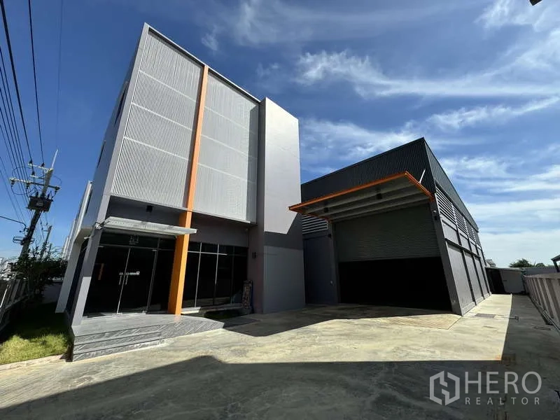 Factory for rent or sale in Lam Luk Ka, Pathum Thani - Front facade of the factory with glass entrance and a covered loading bay with roller shutter.