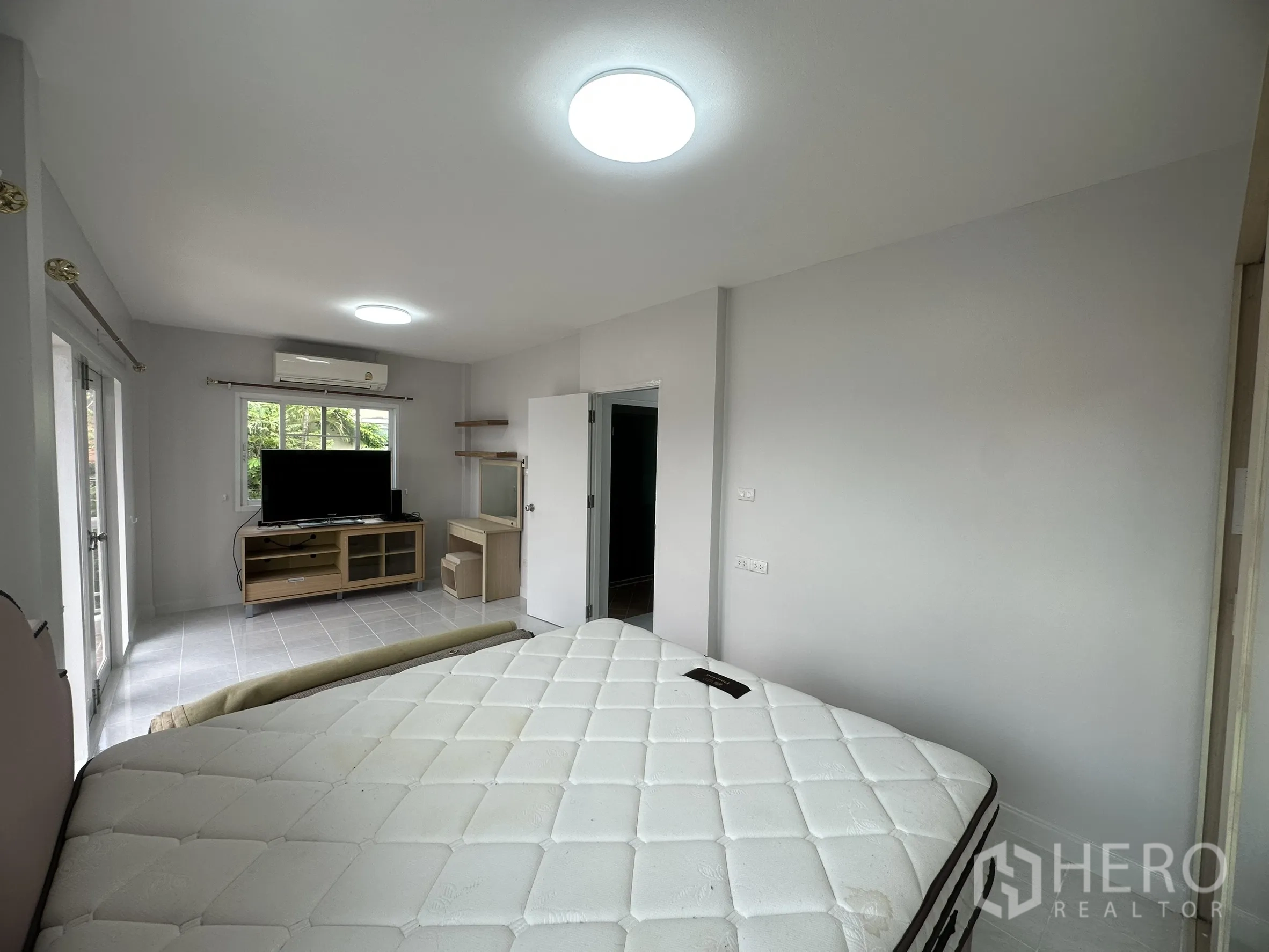 Townhouse for sale in Lam Luk Ka, Pathum Thani - Master bedroom with balcony doors, TV console and air-conditioner.