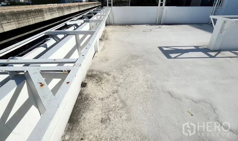 Shophouse for rent in Phra Khanong, Bangkok - Open rooftop terrace with white surface and metal frames beside the elevated rail line.