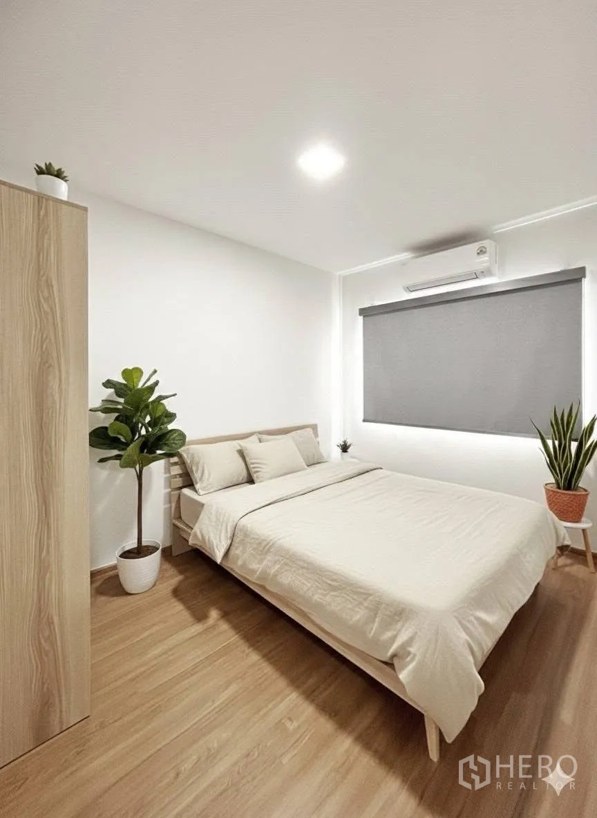 Townhouse for rent in Bang Phli, Samut Prakan - Guest bedroom with double bed, gray roller blind, air conditioner and plants on wood floors.
