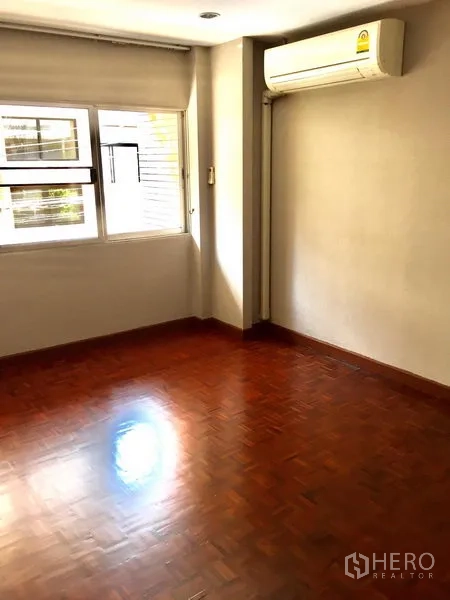 Townhouse for rent in Watthana, Bangkok - Bedroom with corner window, split-type air conditioner and parquet flooring.
