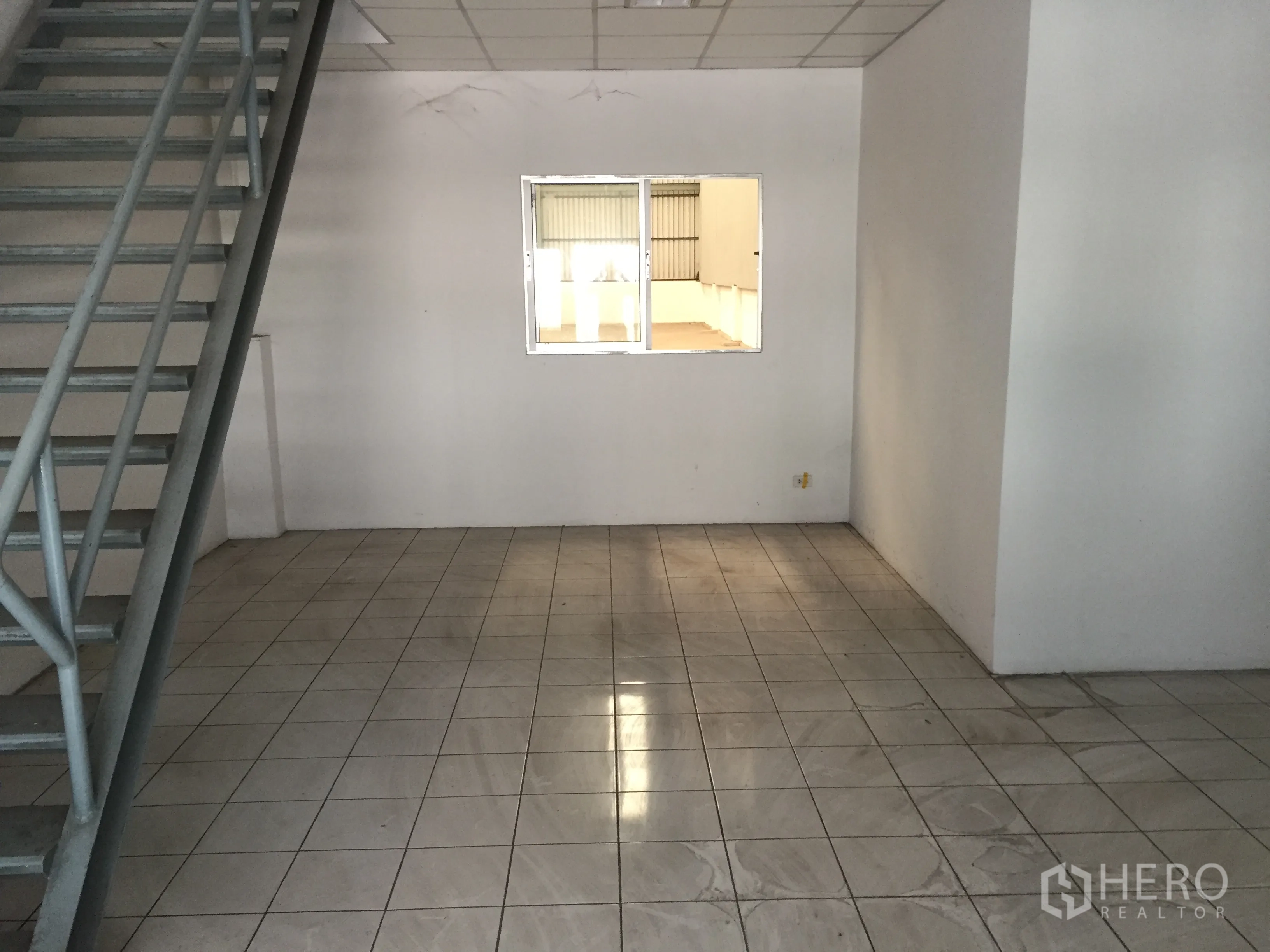 Factory for rent in Khlong Luang, Pathum Thani - Tiled office room with a metal staircase and an interior window overlooking the warehouse.