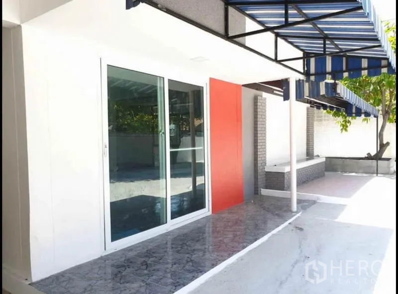 Detached House for rent in Lat Phrao, Bangkok - Covered patio with blue striped awning, red feature wall and full‑height sliding glass doors.